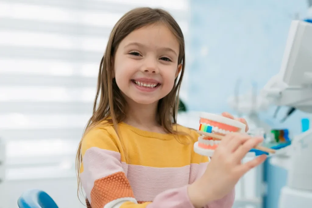 Smiling young girl learning proper brushing techniques with a dental model at crystal clear family dentist in San Antonio.