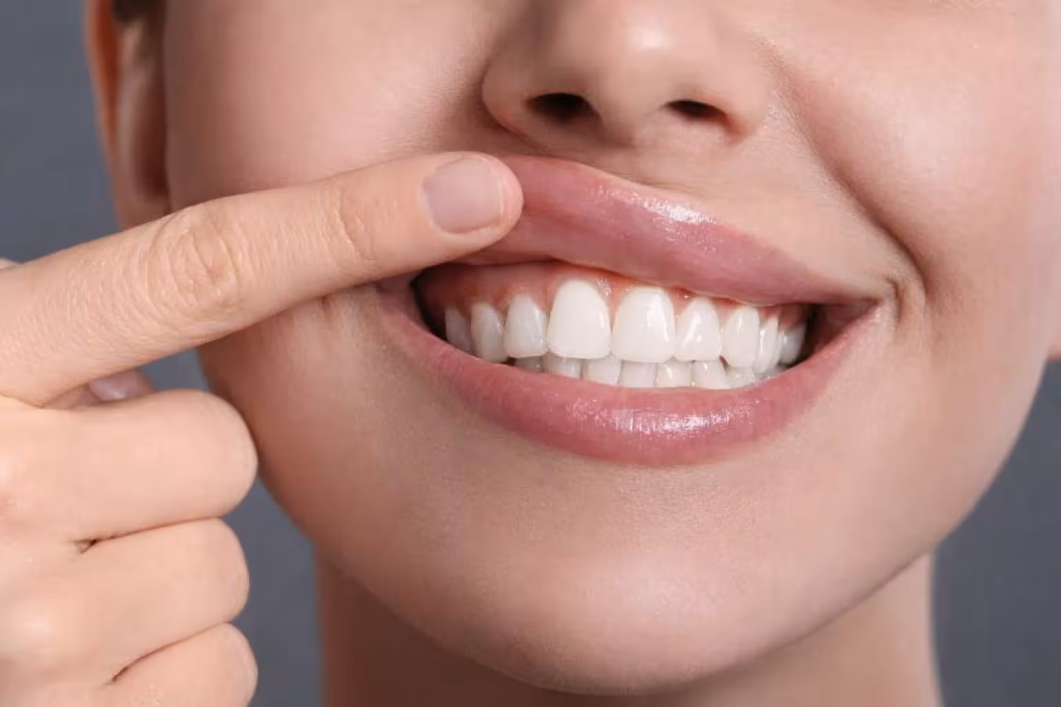 patient pointing at gums and teeth demonstrating crown lengthening results with improved gum line and smile