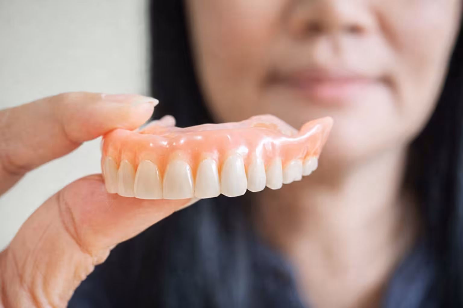 person holding full denture set showing artificial teeth for tooth replacement solution