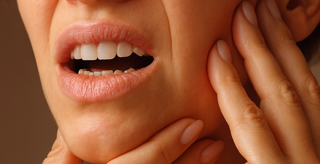 Person pressing jaw in visible discomfort, indicating dental pain or TMJ-related tension.