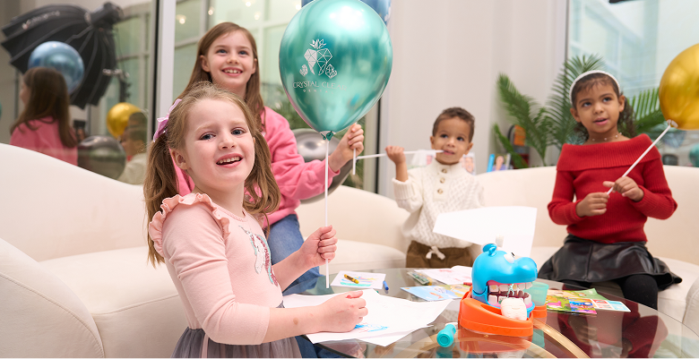 Smiling children engaging in creative play with dental-themed balloons and toys in a bright, kid-friendly dental clinic waiting area.