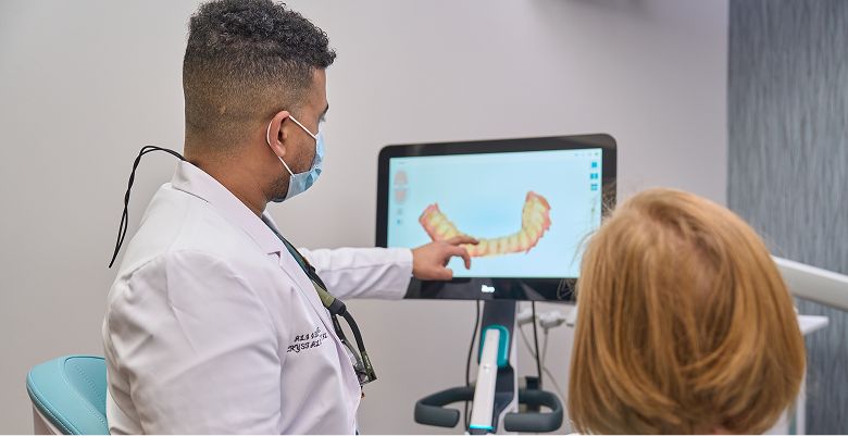Dental professional explains 3D digital model of patient's teeth on computer screen in modern clinic setting