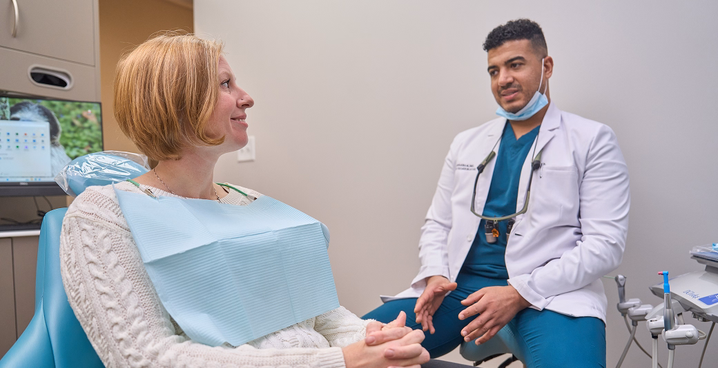 Female patient in dental chair discussing treatment with male dentist in modern clinic setting, surrounded by dental tools and equipment.
