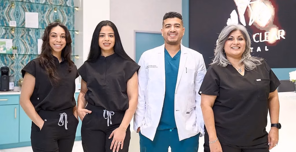 Four dental staff smiling inside a modern clinic.
