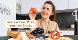 Smiling person in kitchen with tomato, with pizza and breadsticks crossed out for braces-friendly care.