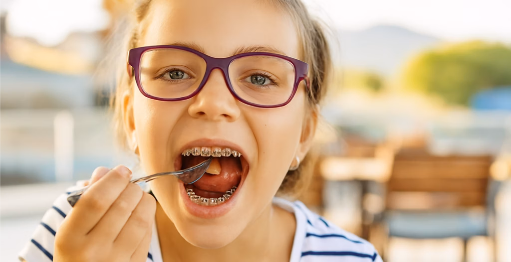 Girl with purple glasses and braces eating with a fork outdoors, highlighting casual dining scene.