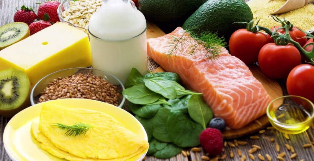 Healthy foods on wood table: salmon, milk, cheese, grains, fruits, veggies, olive oil, and omelet with dill.