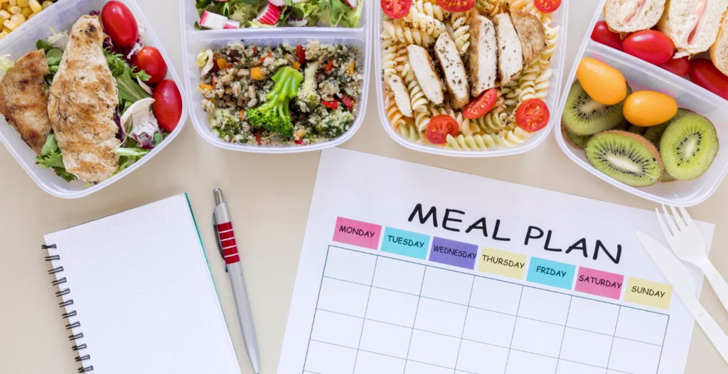 Healthy meal prep containers with chicken, salad, wraps, fruit, and blank weekly meal plan chart with notebook.