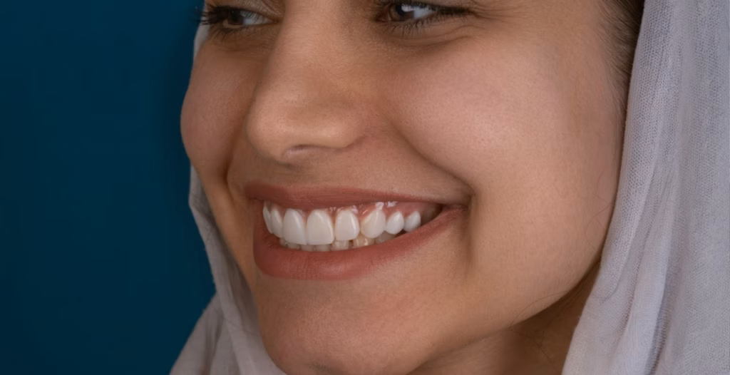 Close-up of a woman smiling, showcasing her clean, straight white teeth against a teal background.
