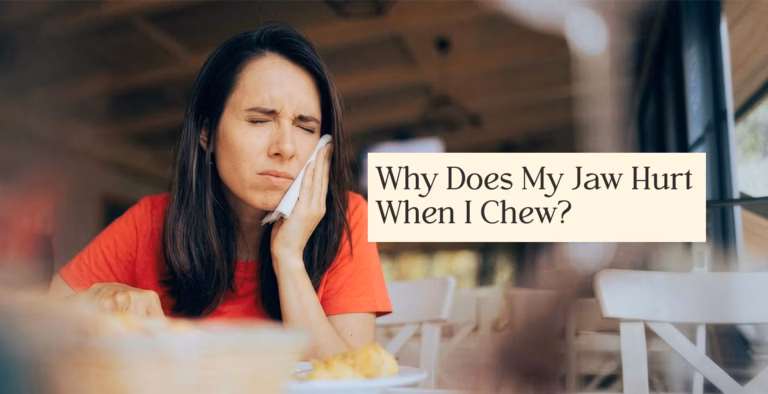Person in red shirt holding jaw in pain while chewing indoors at table.